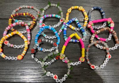 Many colorful beaded bracelets laid out overlapping each other on a black wooden backdrop.