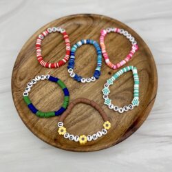 Several colorful handmade beaded bracelets with inspirational words and phrases sitting in a wooden dish on a marble counterop