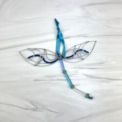silver wire and beads dragonfly ornament with turquoise colors and a turquoise ribbon for hanging laying on a marble counter top