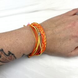 Three part orange anf yellow string bracelet set with tiny metal dragonfly charm on wrist on a white marble countertop