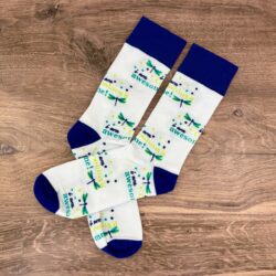 Pair of white knit crew socks with navy blue cuff, heel, and toe and dragonfly logo with "I am awesome" and "I am crushing it" on the white portions in the On A Dragonfly's Wings colors on a wooden countertop