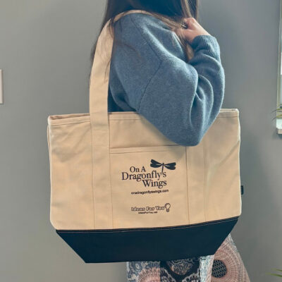 cream colored canvas tote bag large over shoulder of model side view in front of brick wall